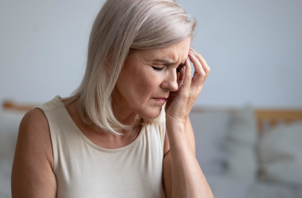 An elderly woman is touching her eye and showing gestures of pain showing in her face.