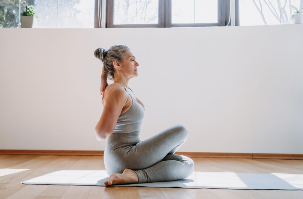 A senior woman in her workout clothes practicing a yoga pose in a brightly lit room.