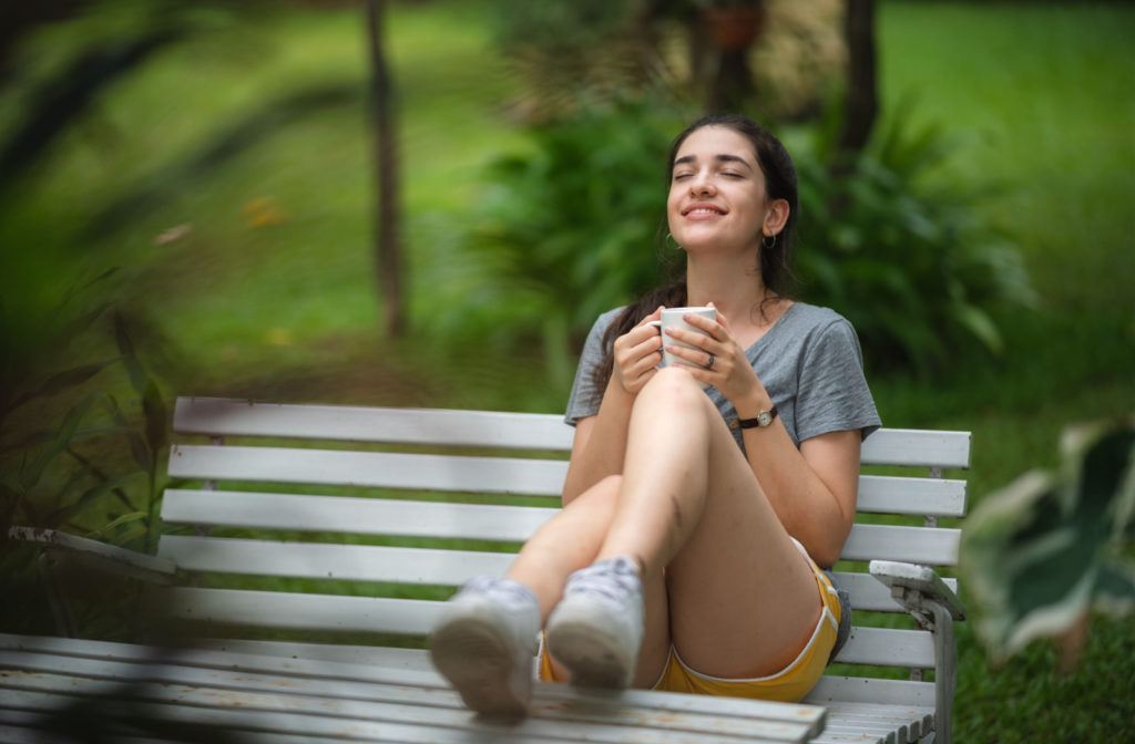 A woman enjoying a cup of hot beverage while sitting on a park bench.