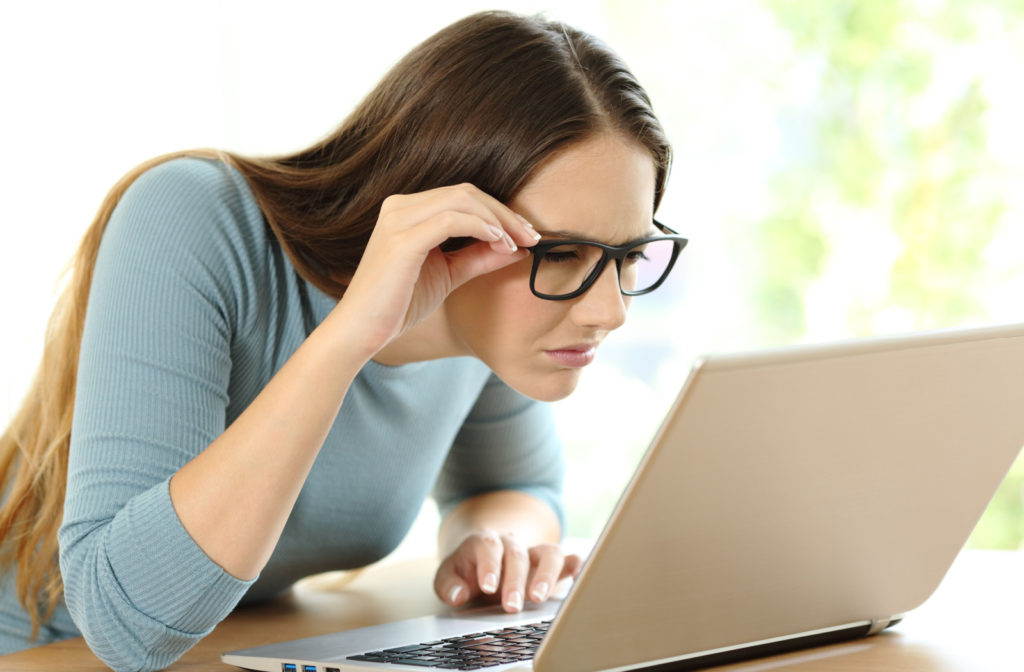 A woman with glasses leaning closer to her laptop screen to see its contents better.