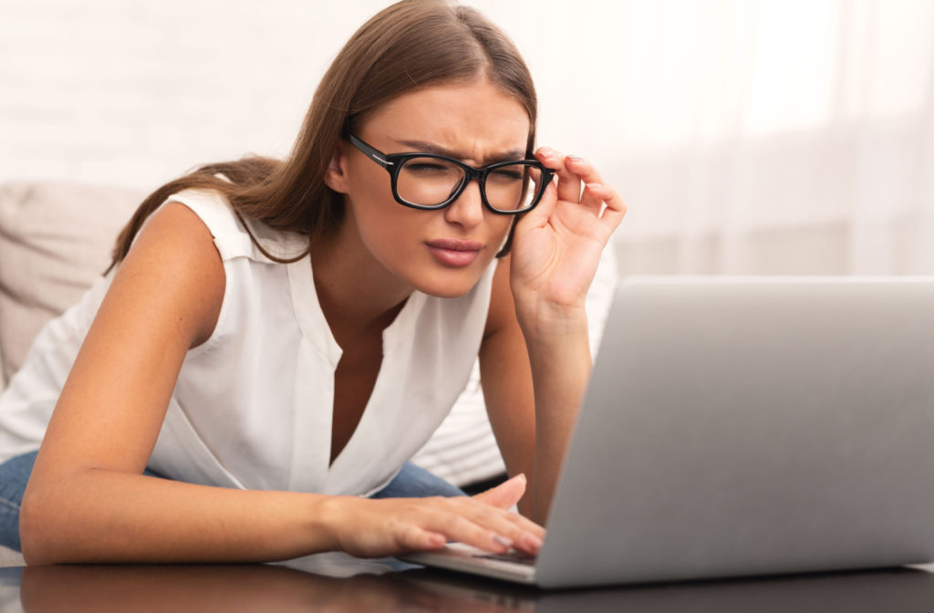 A woman squinting and leaning towards her laptop screen to clearly see its contents.
