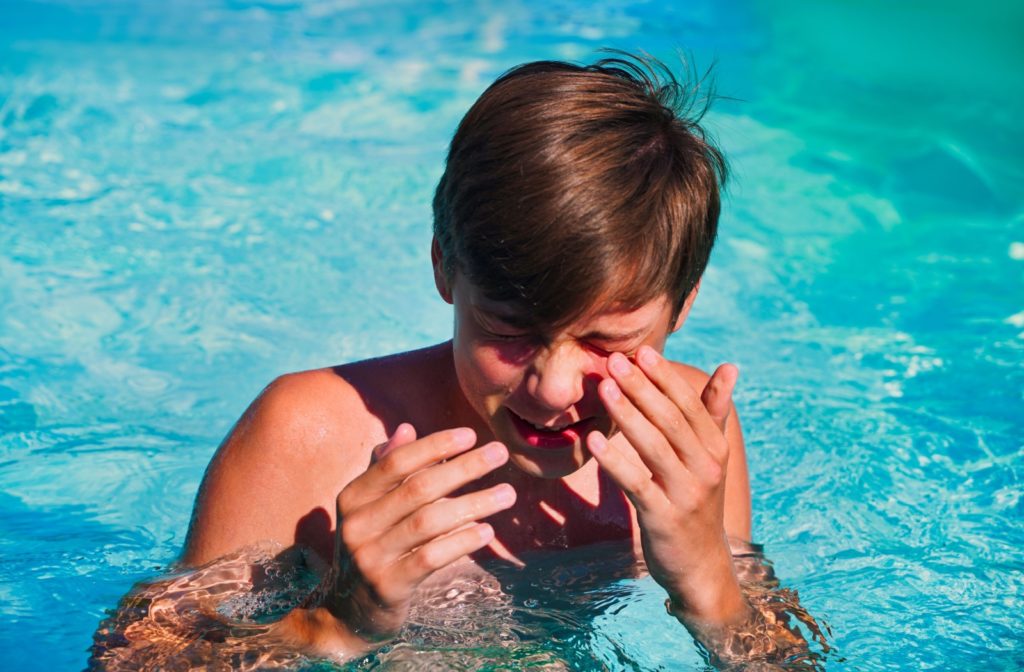 A teenager in the pool wipes their eye due to eye irritation from chlorine.