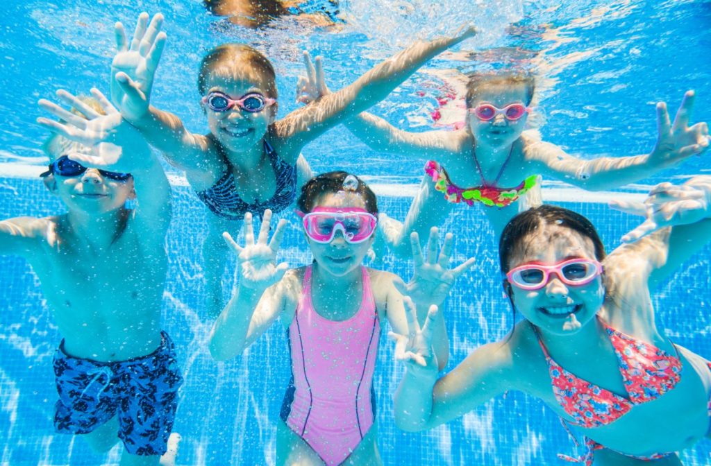 A group of smiling children underwater wearing goggles to prevent blurry vision.