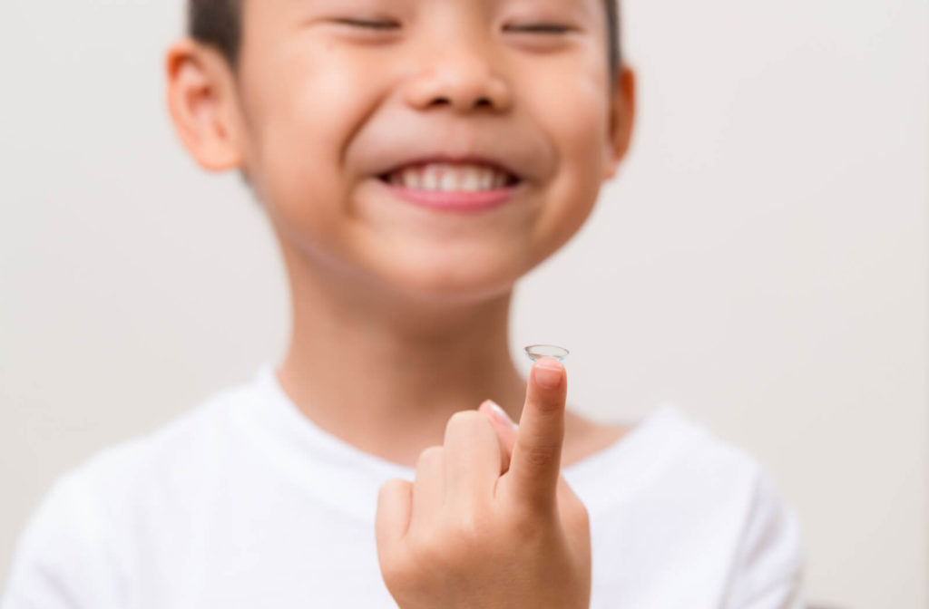 A young child smiles while holding their myopia control contact lens on their finger.