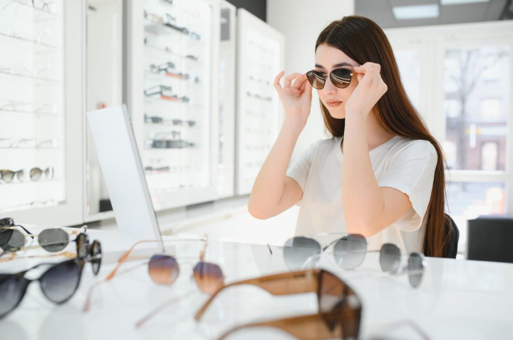 A woman looking in a mirror while trying on different styles of sunglasses.