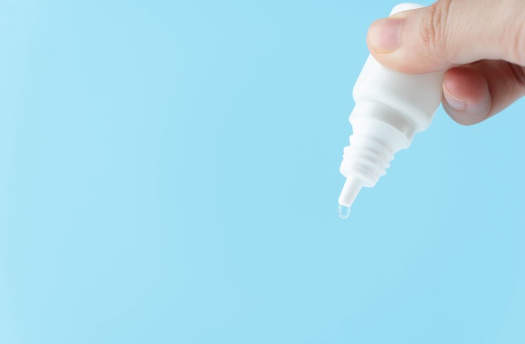 A handing squeezing a bottle of eye drops in front of a blue background.