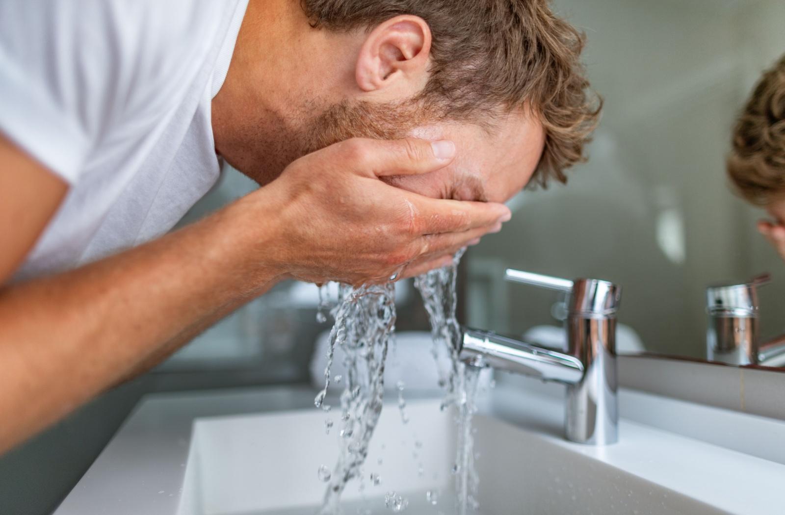 A person flushing their eyes with water in the bathroom as an alternative to rubbing their eyes.