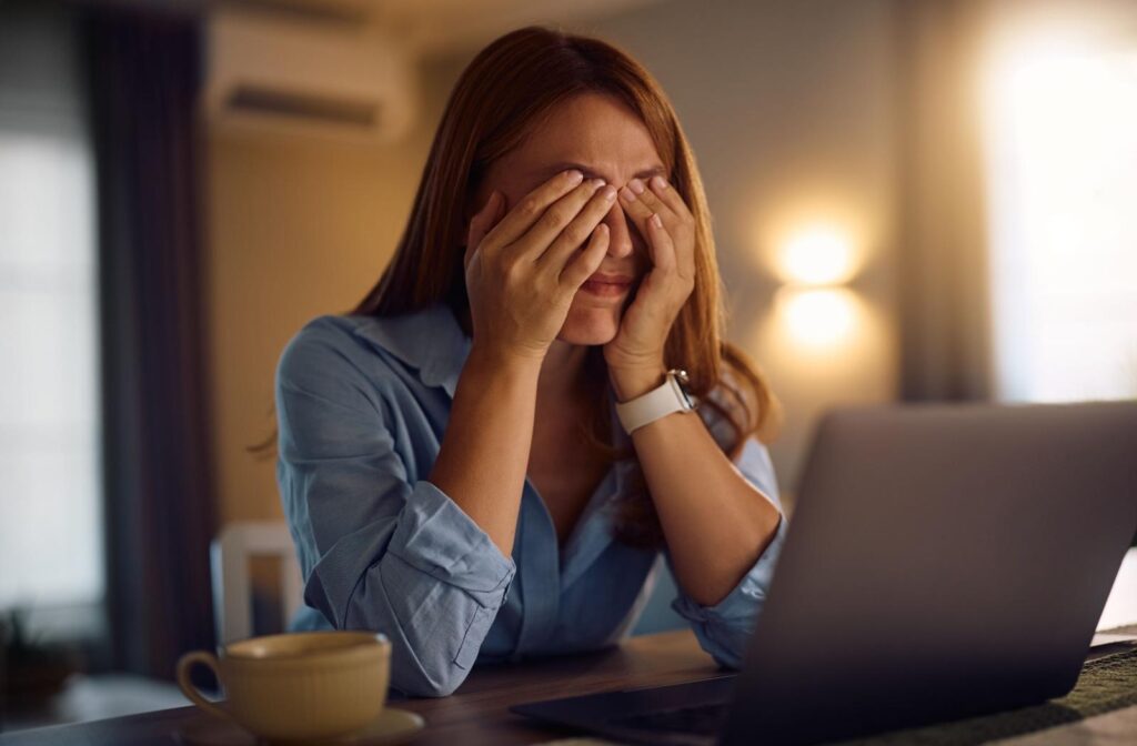 A person sitting in front of their laptop rubbing their eyes.